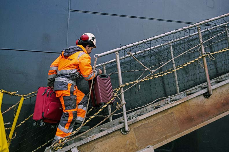 Marlow Navigation crew member in Hapag-Lloyd uniform boarding a ship with suitcases.